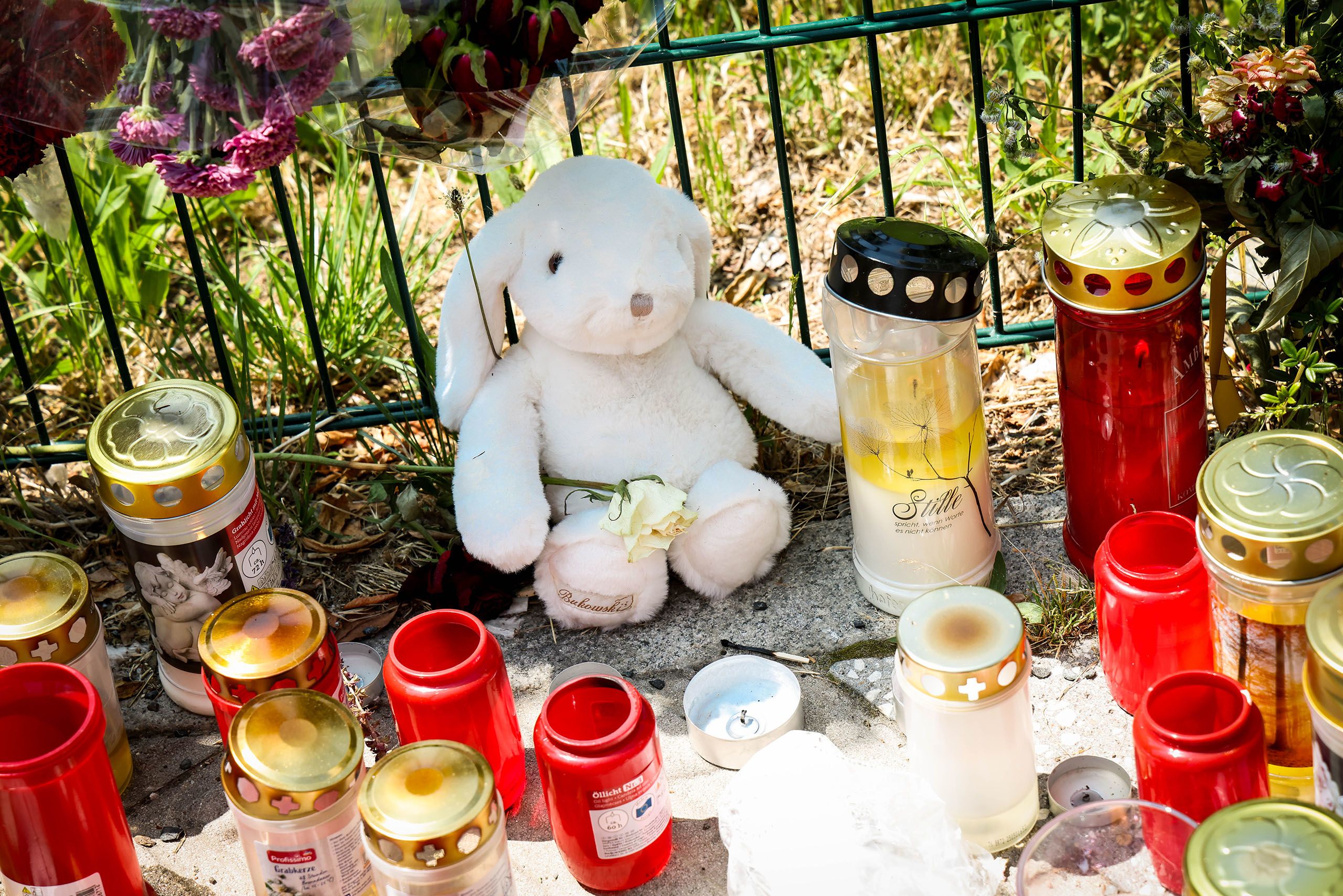 Ein Stofftierhase sitzt inmitten von Grabkerzen und hält eine weiße Rose.