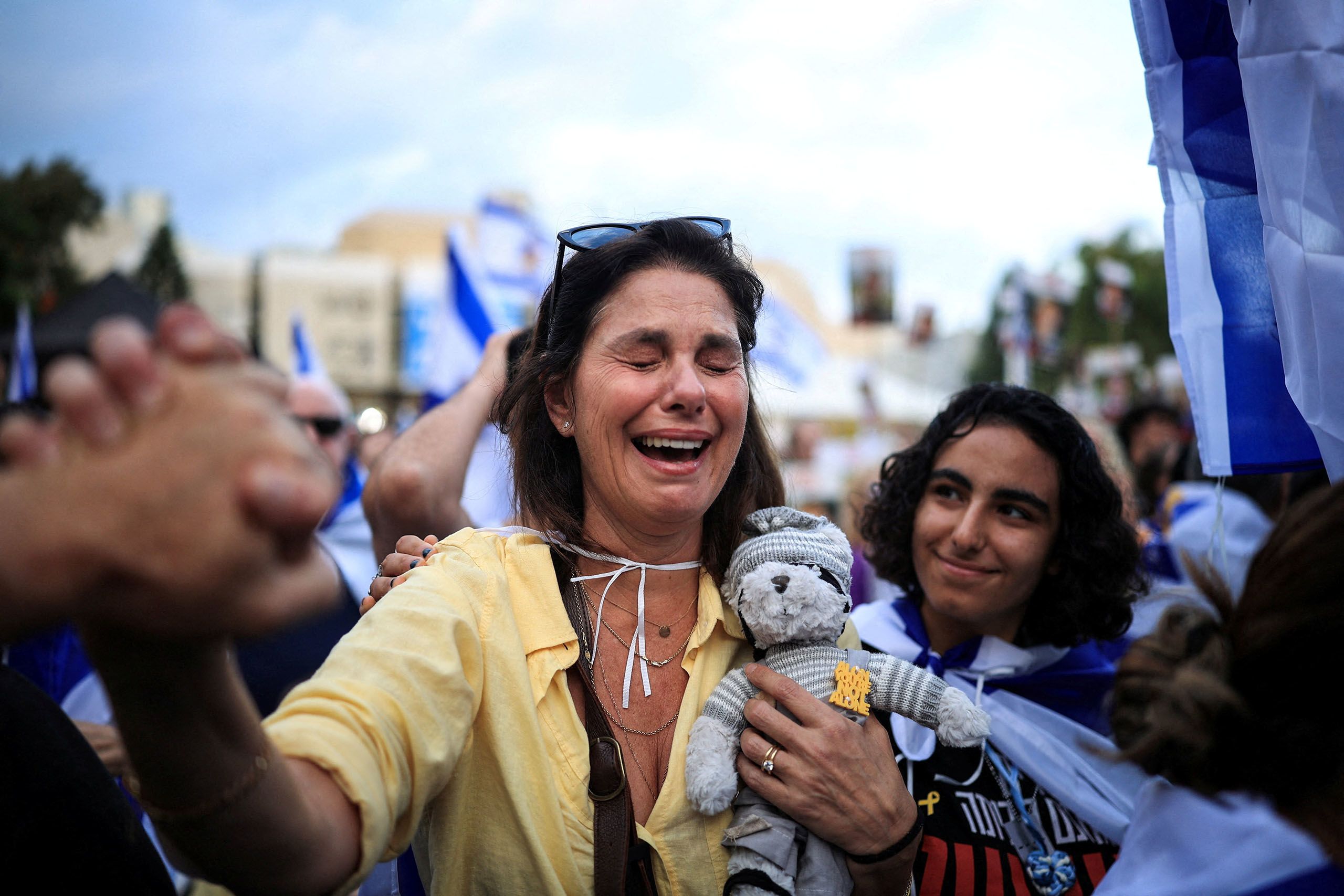 Eine Frau mit gelber Bluse lacht sichtlich erleichtert. Sie trägt dabei ein Stofftier, hat die Augen geschlossen und hält eine Hand. Daneben ein junger Mann.
