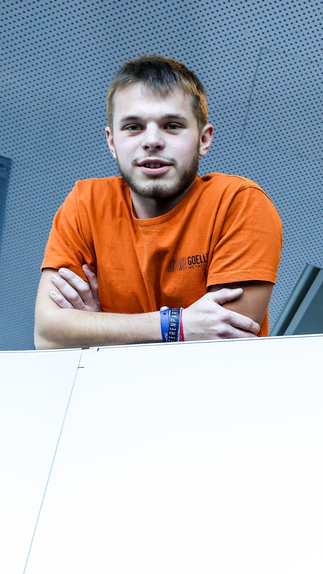 Der Lehrling trägt ein oranges T-Shirt und posiert für das Foto, auf seine Unterarme gestützt.