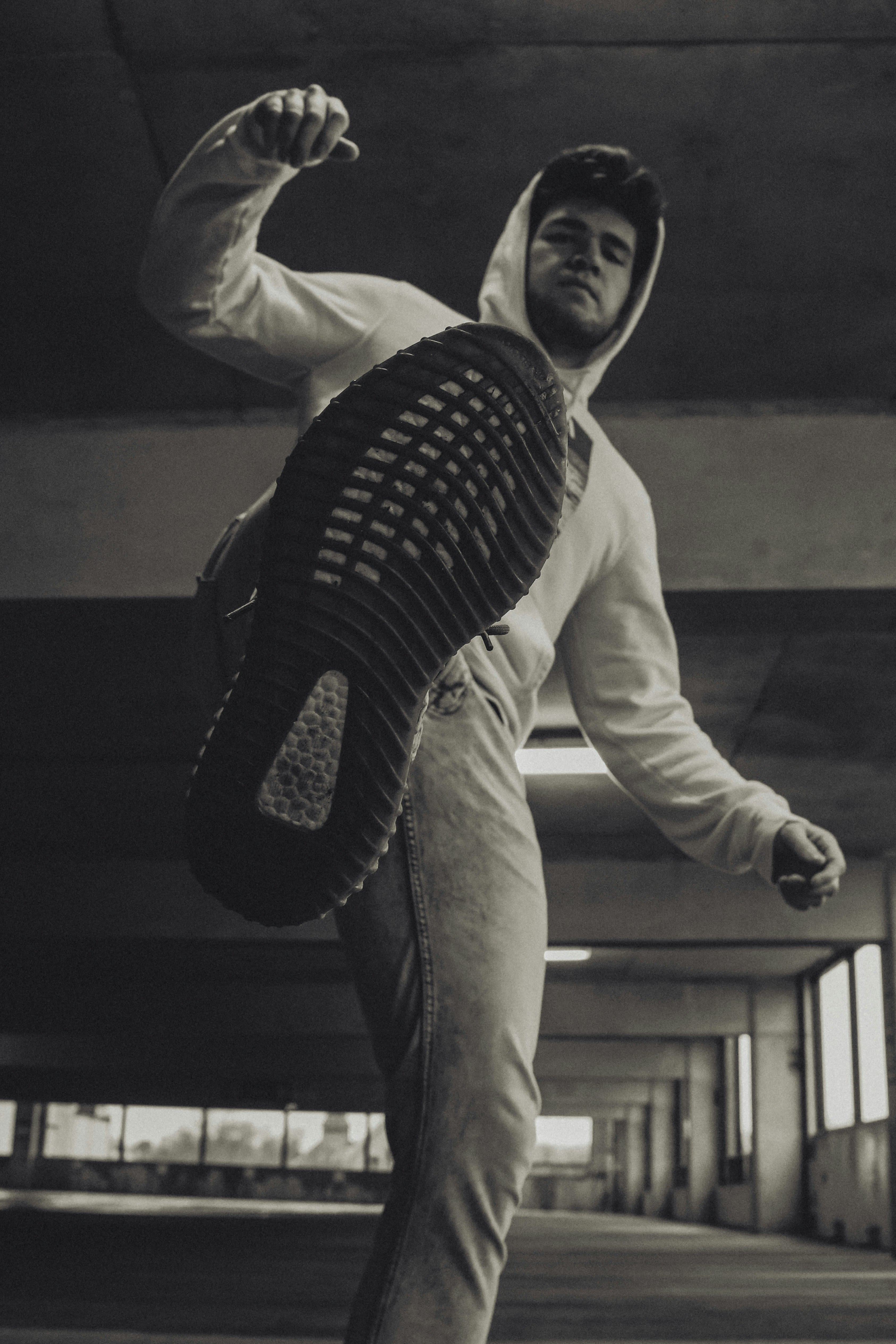 Junger Mann mit Kapuzenpulli hebt das Bein und tritt mit dem Fuß Richtung Kamera.