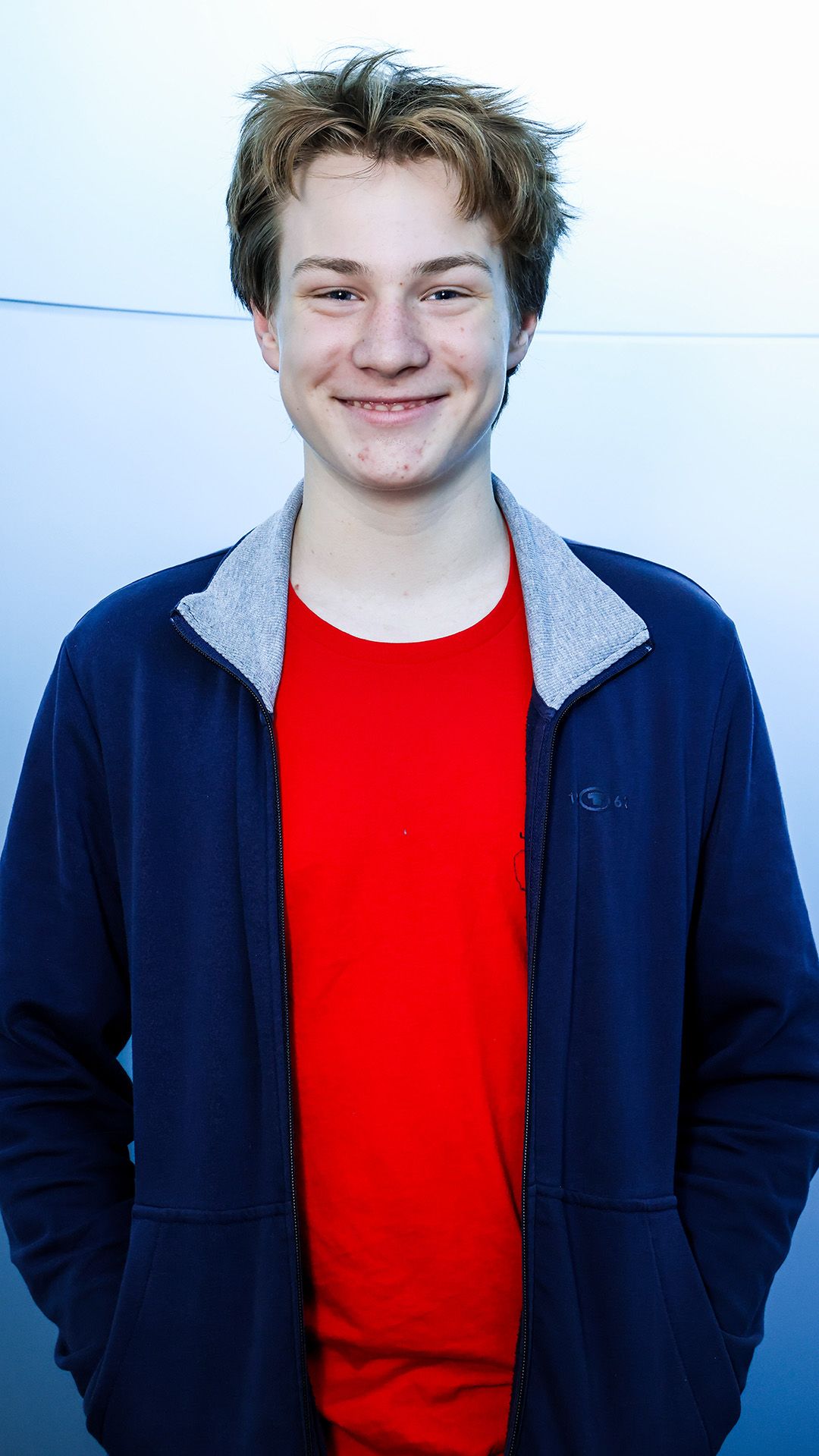 Der Schüler trägt ein rotes T-Shirt und eine blaue Jacke und posiert für das Foto.
